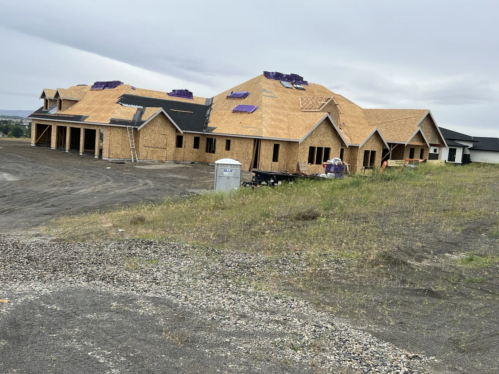 Large custom home with hip roof and dormers, dried in with underlayment overlooking the valley