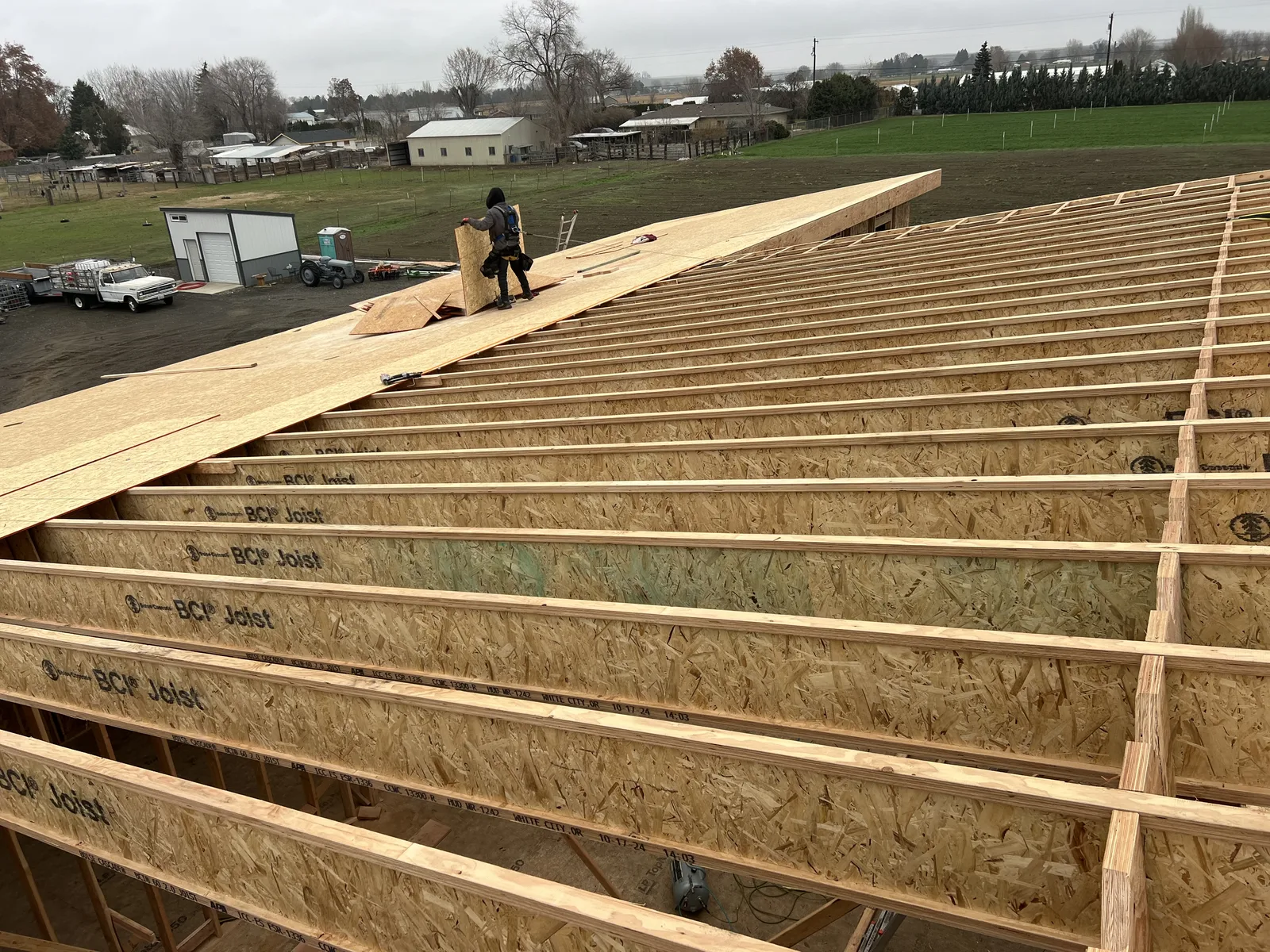 Aerial view of roof sheathing installation with exposed BCI I-joists on a modern shed-roof custom home