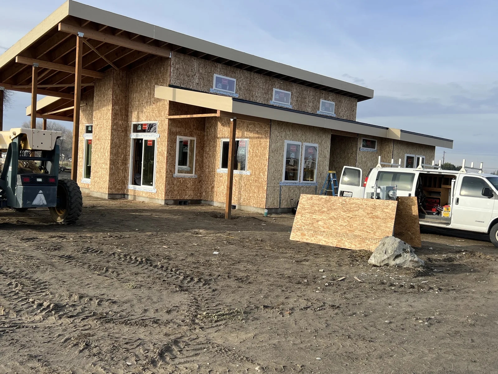 Modern custom home exterior at golden hour with windows installed and covered entry framing